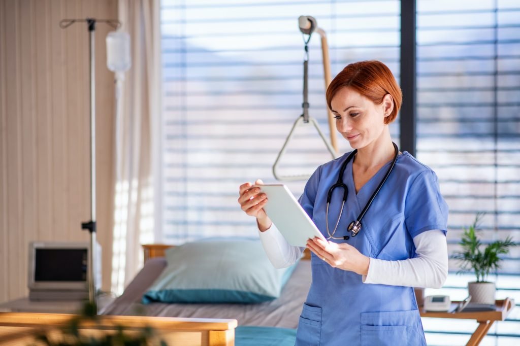 Portrait of female doctor or nurse standing in hospital room, using tablet